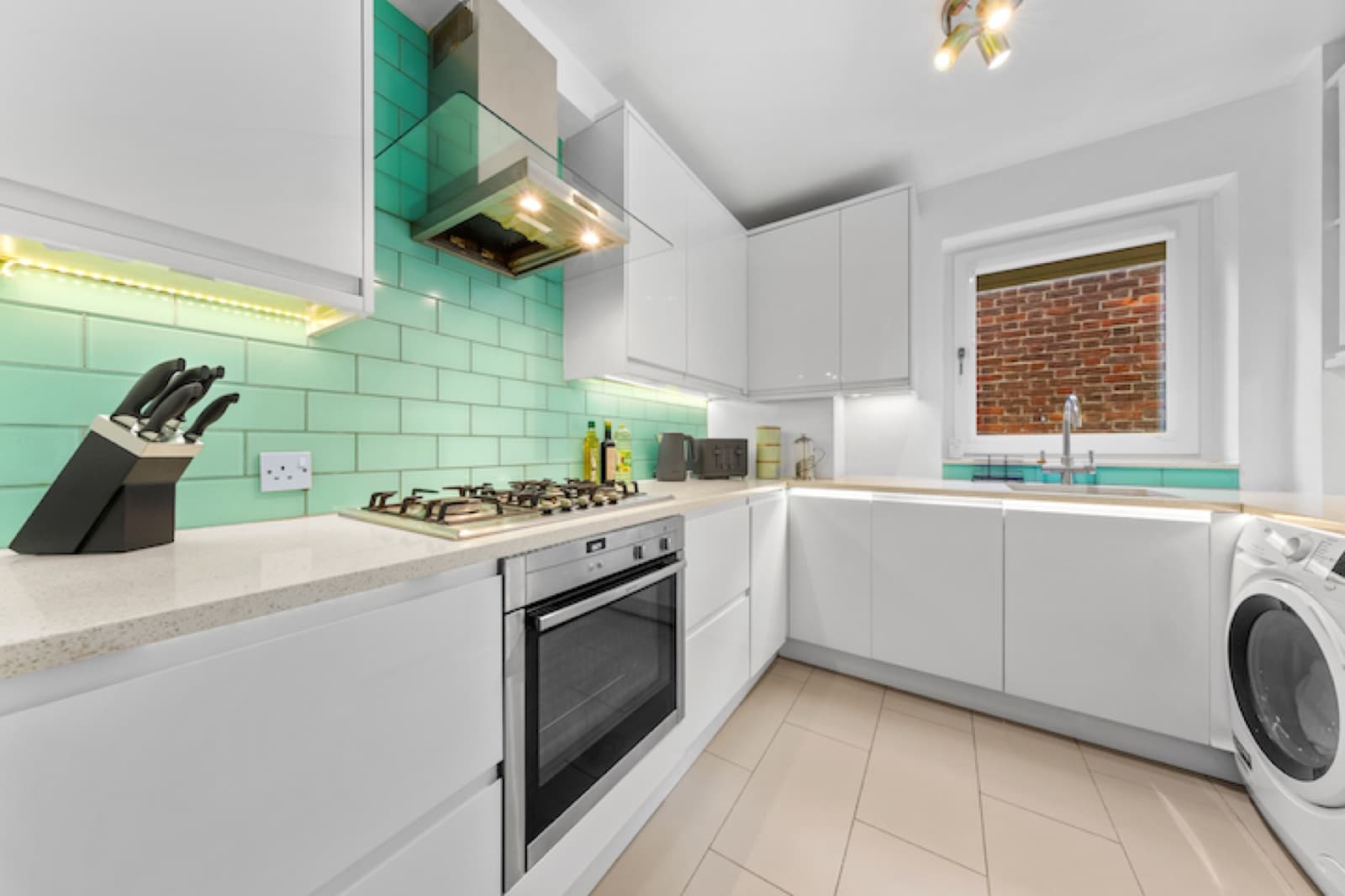 A finished kitchen with teal tiles, gas hob and integrated oven